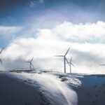 Wind Turbines in the distance, looking over snowy hills towards blue and cloudy skies