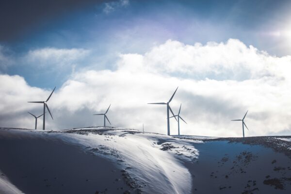 Wind Turbines in the distance, looking over snowy hills towards blue and cloudy skies