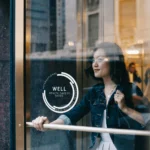 A woman walking out of a glass door from a building with the WELL logo on the glass