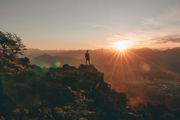 A person standing on a rock looking at the sunset out to the distant horizon